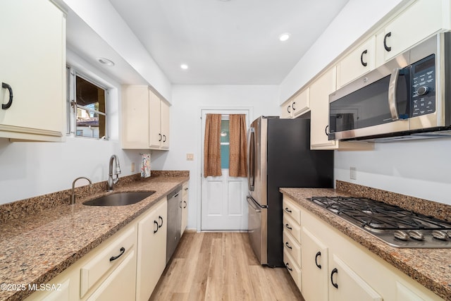 kitchen with cream cabinetry, light wood finished floors, appliances with stainless steel finishes, a sink, and dark stone counters