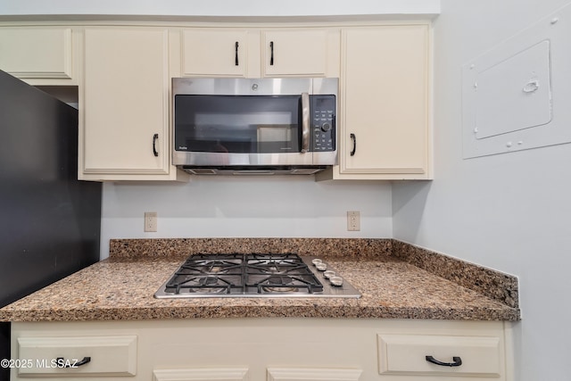 kitchen featuring cream cabinets, electric panel, stainless steel appliances, and dark stone countertops