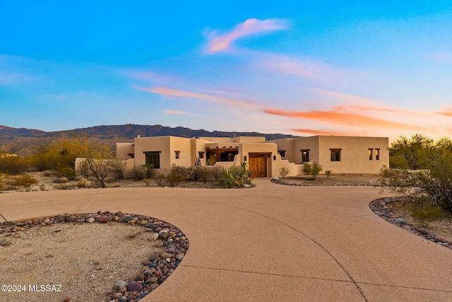 pueblo-style house with curved driveway, a mountain view, and stucco siding