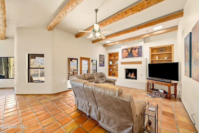 living area featuring built in shelves, beam ceiling, light tile patterned floors, a ceiling fan, and a warm lit fireplace