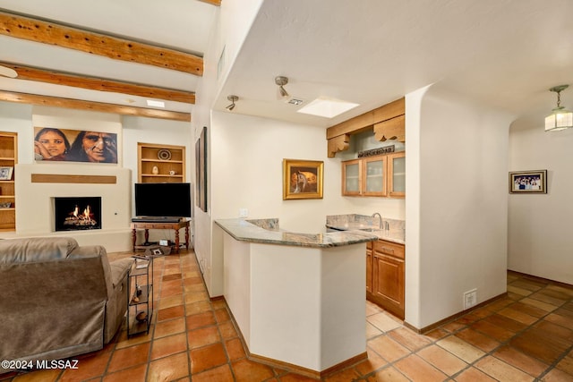 kitchen with open floor plan, a lit fireplace, brown cabinets, beamed ceiling, and glass insert cabinets