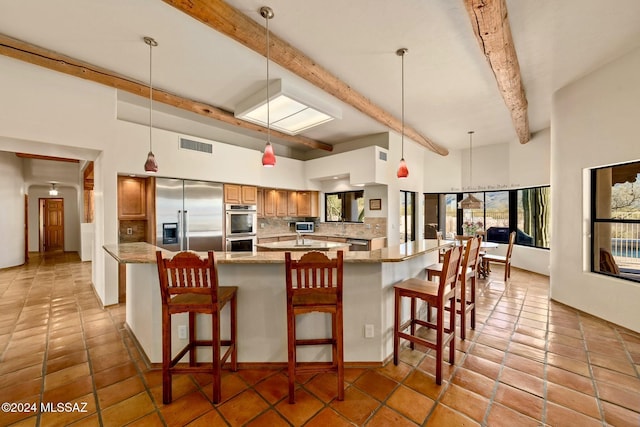 kitchen featuring stainless steel appliances, pendant lighting, brown cabinets, and light stone countertops