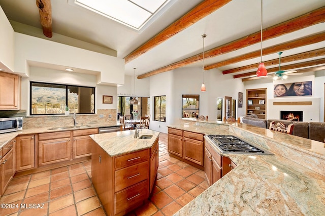 kitchen with stainless steel appliances, a sink, open floor plan, light stone countertops, and a center island with sink