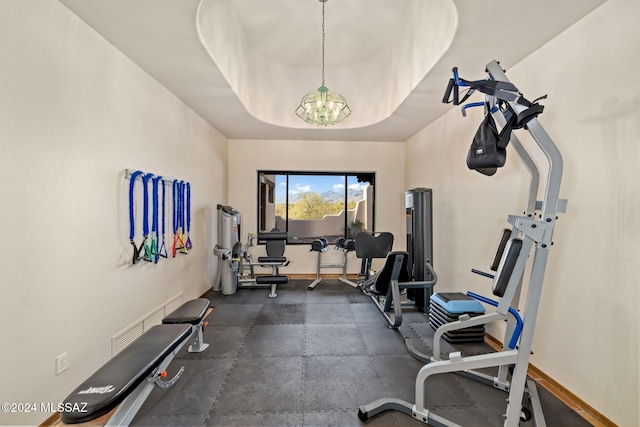 workout room featuring a chandelier, a tray ceiling, and baseboards