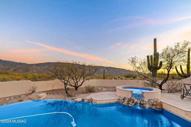 pool at dusk featuring a fenced in pool, a fenced backyard, a mountain view, and an in ground hot tub