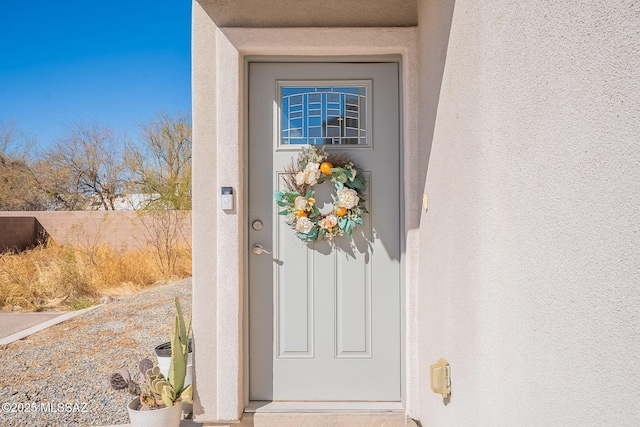 entrance to property featuring fence and stucco siding