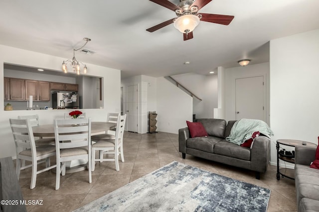 living room with ceiling fan with notable chandelier, visible vents, and light tile patterned flooring