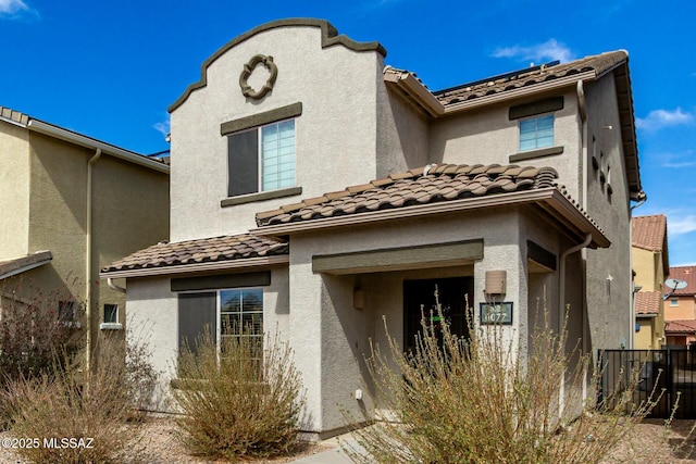 view of front facade featuring fence, a tiled roof, and stucco siding