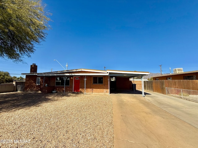 ranch-style house with brick siding, a chimney, concrete driveway, fence, and an attached carport