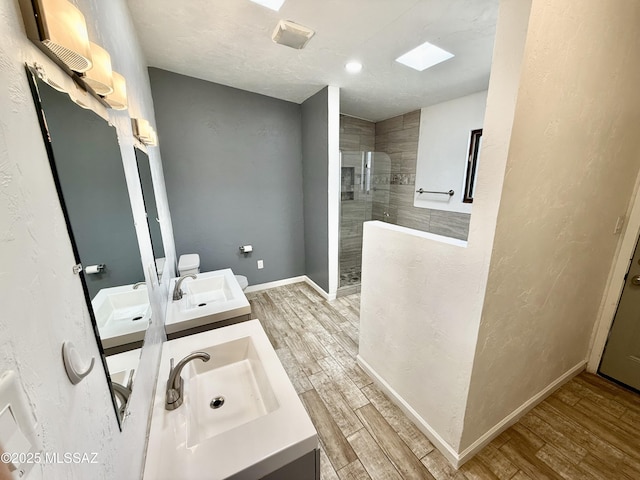 bathroom with a walk in shower, wood finished floors, a sink, baseboards, and double vanity