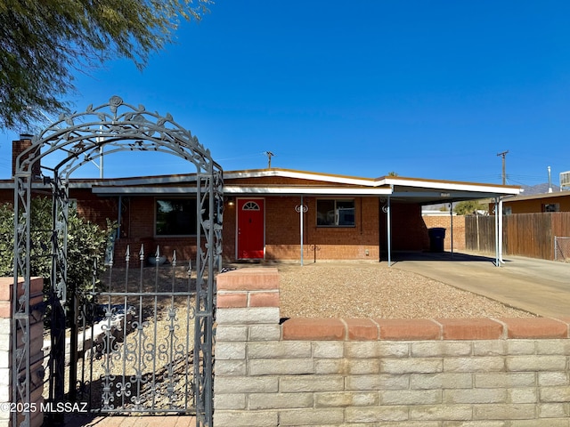 view of front of property featuring a carport, concrete driveway, brick siding, and a fenced front yard