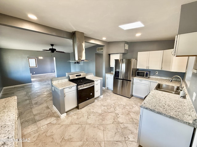 kitchen featuring appliances with stainless steel finishes, open floor plan, white cabinets, a sink, and island range hood