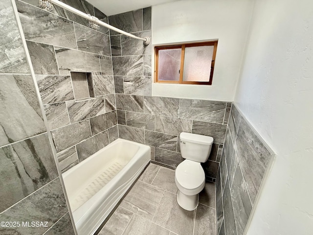 full bath featuring toilet, a tile shower, and tile walls