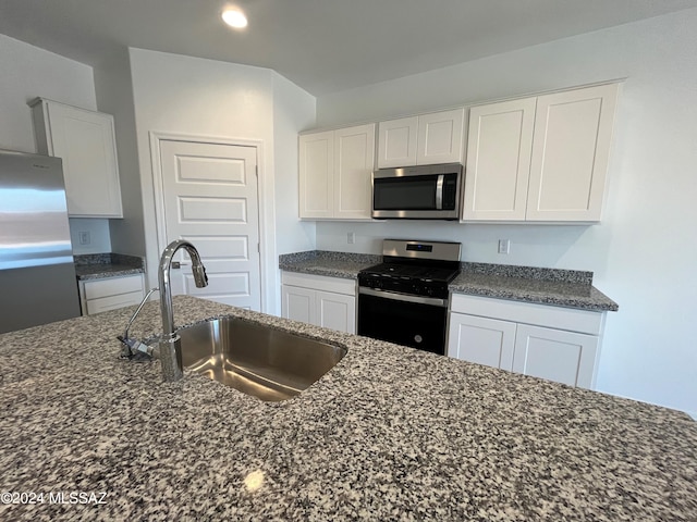 kitchen featuring white cabinets, dark stone countertops, stainless steel appliances, and a sink