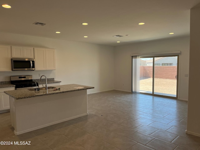 kitchen featuring white cabinets, light stone counters, appliances with stainless steel finishes, a kitchen island with sink, and a sink