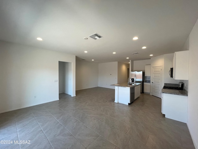 kitchen with a center island with sink, visible vents, open floor plan, white cabinetry, and dark stone counters