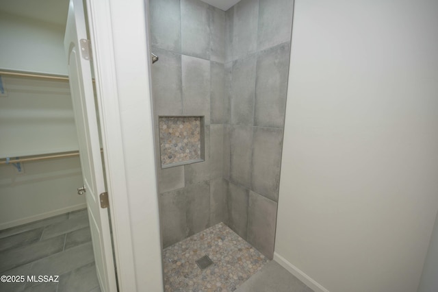 bathroom with a spacious closet, tiled shower, and baseboards