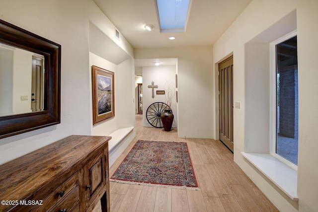 hallway with a skylight, visible vents, and light wood-style floors