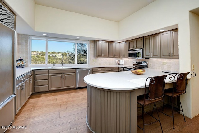 kitchen with a peninsula, light wood finished floors, appliances with stainless steel finishes, and backsplash