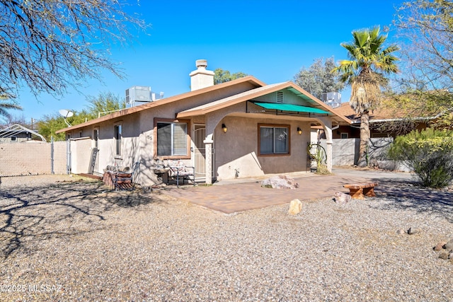 view of front facade featuring a patio, a chimney, fence, and stucco siding