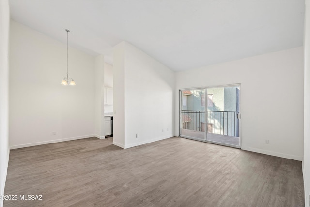 empty room with lofted ceiling, a notable chandelier, baseboards, and wood finished floors