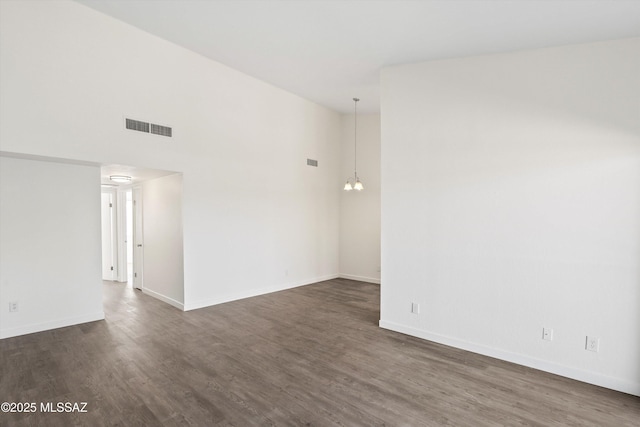 unfurnished room with a towering ceiling, baseboards, visible vents, and dark wood-type flooring