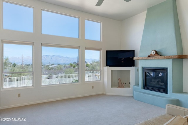 unfurnished living room with a large fireplace, baseboards, ceiling fan, a high ceiling, and carpet flooring