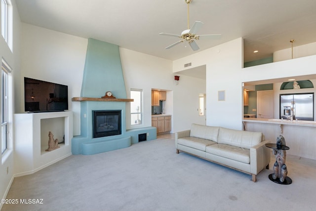 living room featuring a towering ceiling, a fireplace, and light colored carpet