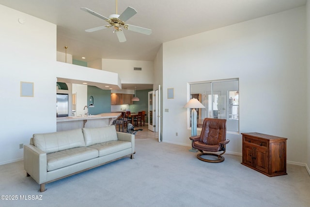 living room with light carpet, visible vents, baseboards, a towering ceiling, and a ceiling fan