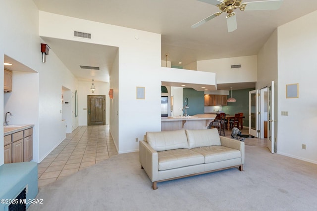 living area with light tile patterned floors, light colored carpet, a ceiling fan, a towering ceiling, and visible vents