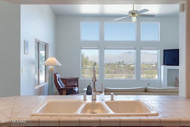 kitchen featuring a ceiling fan, a high ceiling, tile counters, and a sink