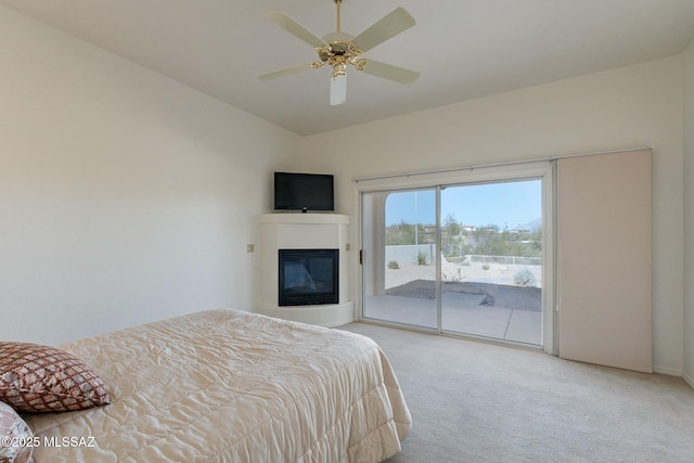 bedroom with access to exterior, lofted ceiling, a glass covered fireplace, light carpet, and ceiling fan