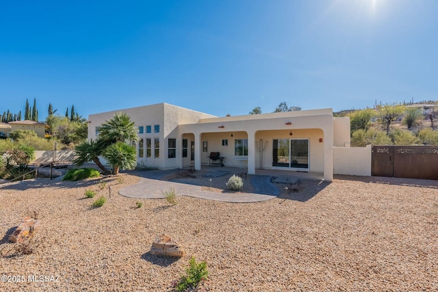 rear view of house with a patio area, fence, and stucco siding