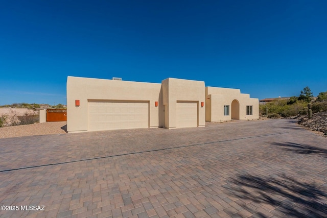 adobe home with decorative driveway, fence, and stucco siding