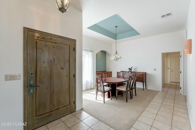 dining area with arched walkways, a tray ceiling, light tile patterned floors, light colored carpet, and visible vents