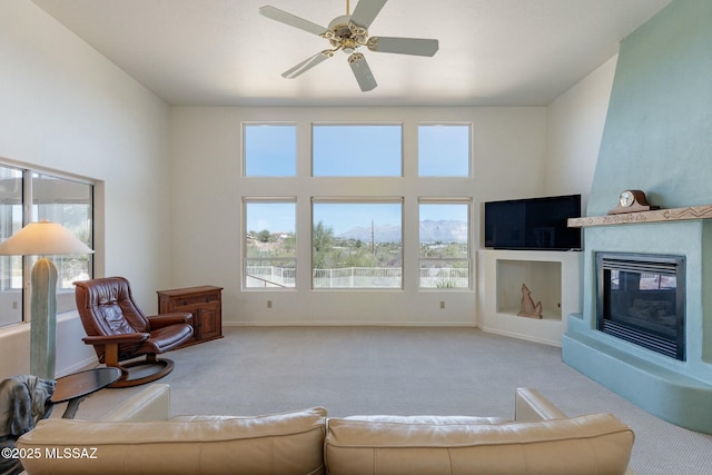 living area with light carpet, ceiling fan, a glass covered fireplace, and baseboards