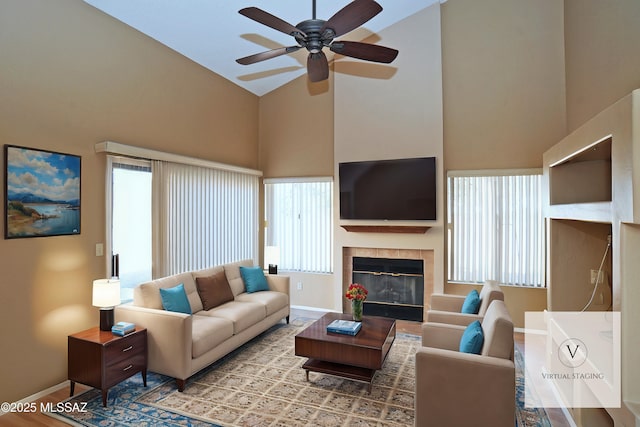 living room featuring ceiling fan, high vaulted ceiling, a fireplace, and baseboards