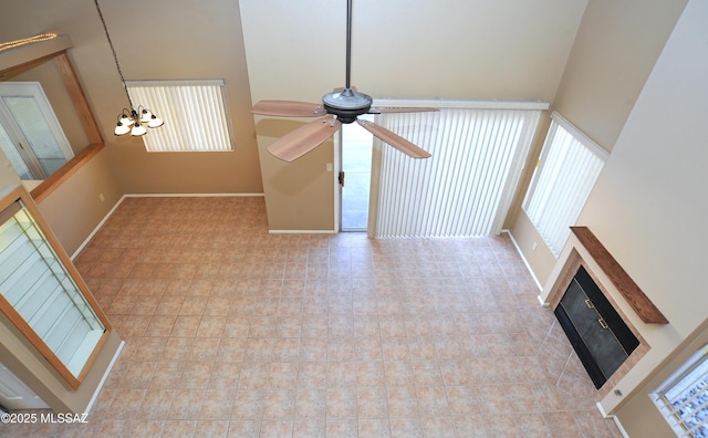 unfurnished living room with ceiling fan with notable chandelier, a high ceiling, a glass covered fireplace, and baseboards