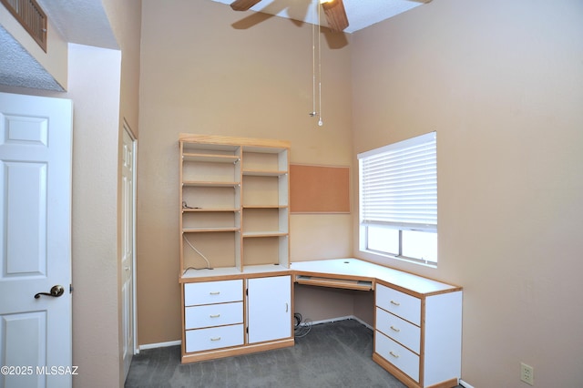 unfurnished office featuring ceiling fan, dark carpet, and built in study area