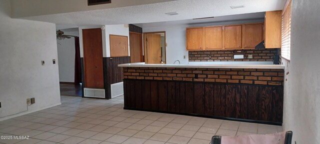 kitchen with a textured ceiling, a peninsula, visible vents, a ceiling fan, and light countertops