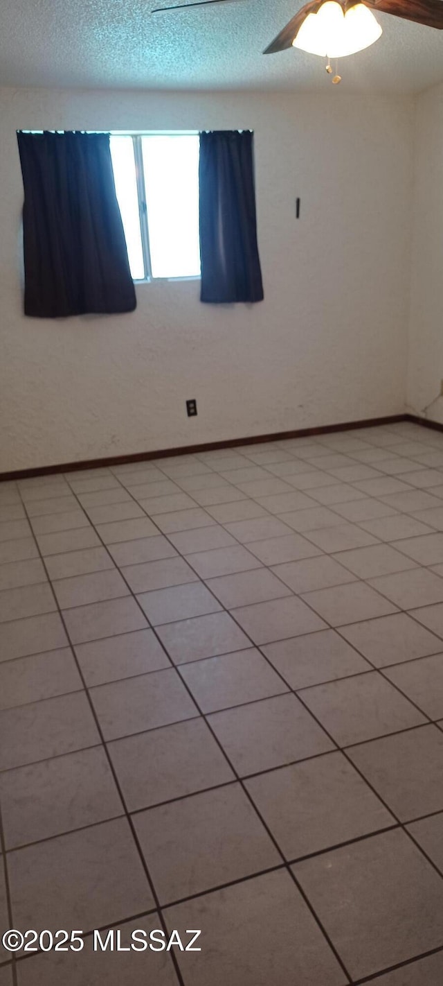 empty room with a textured ceiling, a ceiling fan, and baseboards