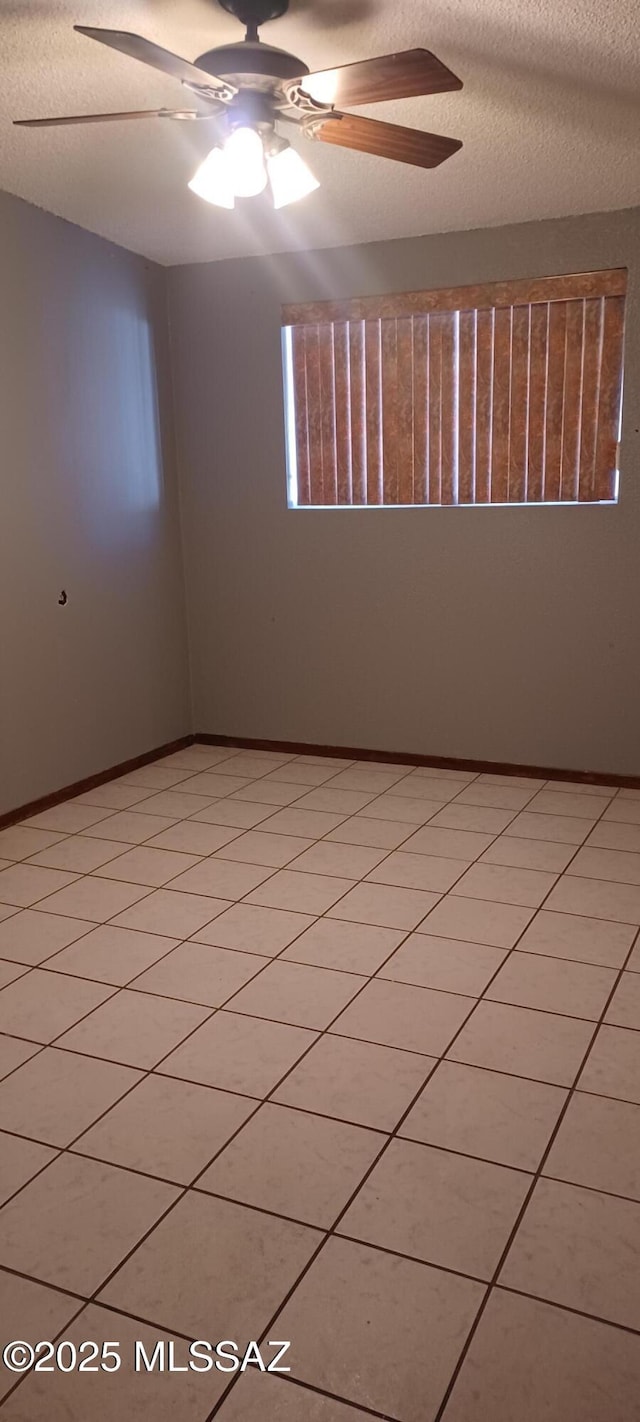 unfurnished room featuring a textured ceiling, ceiling fan, light tile patterned floors, and baseboards