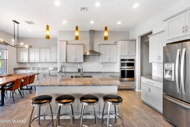 kitchen with visible vents, appliances with stainless steel finishes, a breakfast bar, wall chimney range hood, and a sink