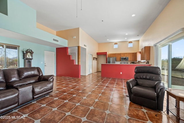 living area with recessed lighting, a healthy amount of sunlight, visible vents, and a towering ceiling