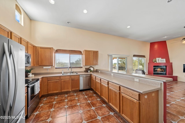 kitchen featuring a peninsula, a sink, stainless steel appliances, a fireplace, and a wealth of natural light