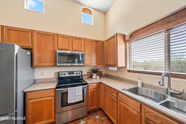 kitchen with a high ceiling, stainless steel appliances, light countertops, dark tile patterned floors, and a sink