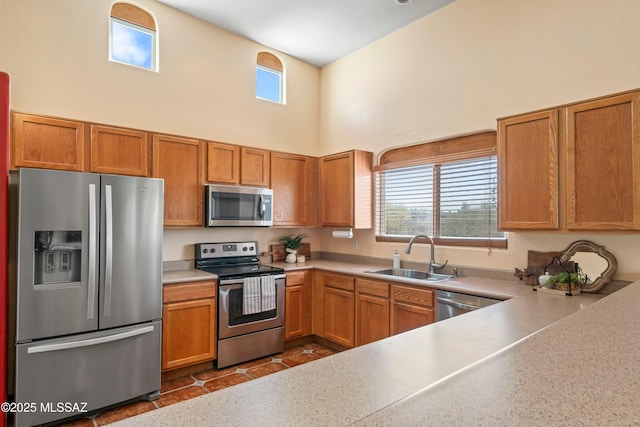 kitchen featuring a high ceiling, a sink, light countertops, appliances with stainless steel finishes, and brown cabinetry