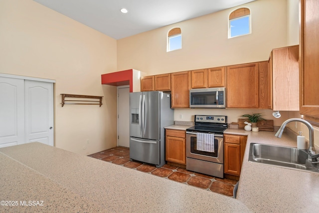 kitchen featuring a high ceiling, a sink, light countertops, appliances with stainless steel finishes, and brown cabinetry