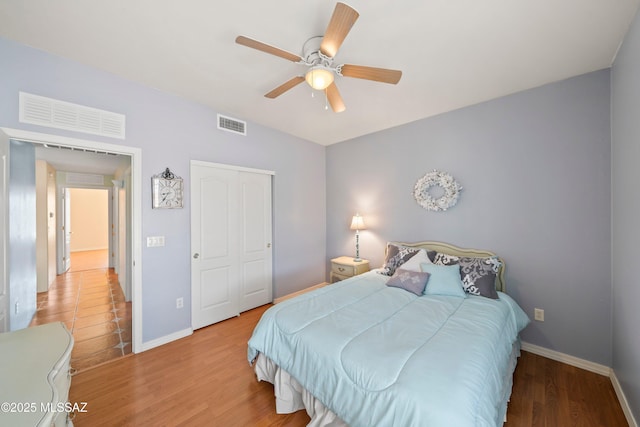 bedroom with a ceiling fan, wood finished floors, visible vents, and baseboards