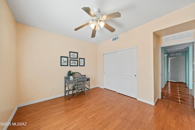 unfurnished office featuring light wood-style floors, visible vents, baseboards, and a ceiling fan